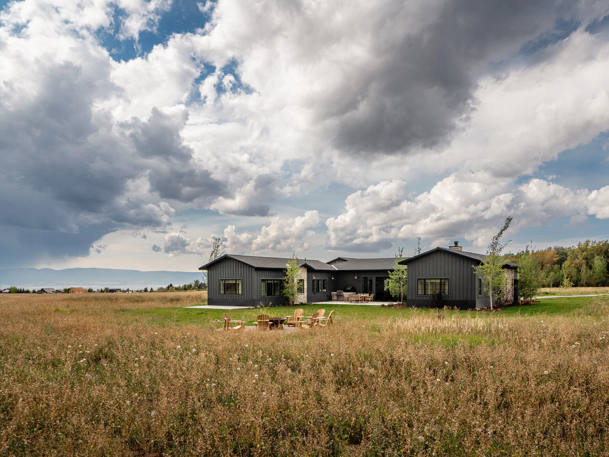 Exterior view of the home beneath dramatic clouds with the fire pit in the foreground — architectural photography Driggs Idaho, River's Edge